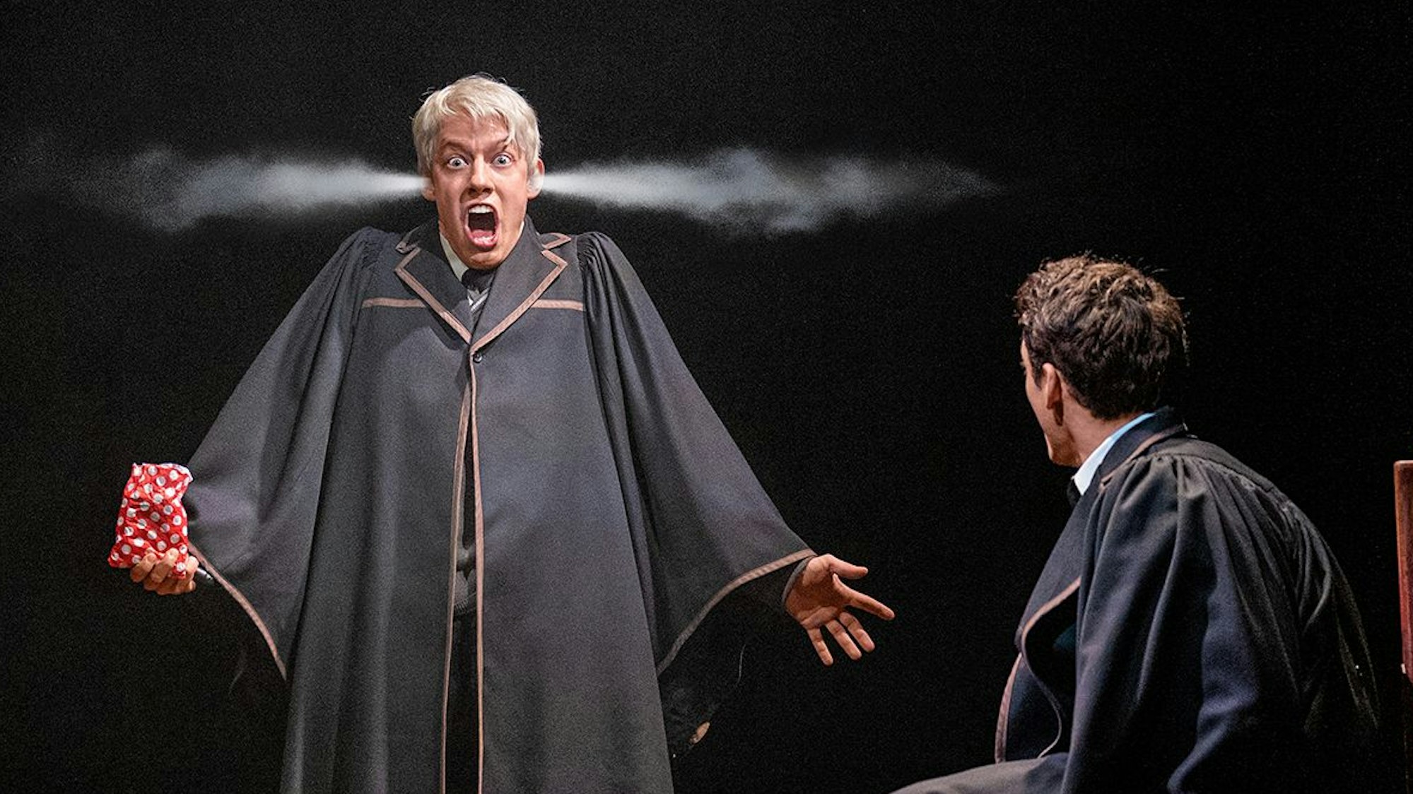 Scorpuis Malfoy und Albus Dumbledore Potter sind zusammen in einem Abteil des Hogwarts-Express. Albus sitzt und schaut zu Scorpius, der zwischen den Sitzen steht. Aus seinen Ohren kommt Rauch, sein Mund ist weit geöffnet, in seiner Hand hält er eine Tüte mit Süßigkeiten. Beide tragen Hogwarts-Schuluniformen.