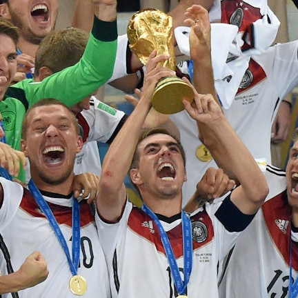 Philipp Lahm jubelt mit dem WM-Pokal zwischen seinen Teamkollegen Lukas Podolski und Thomas Müller