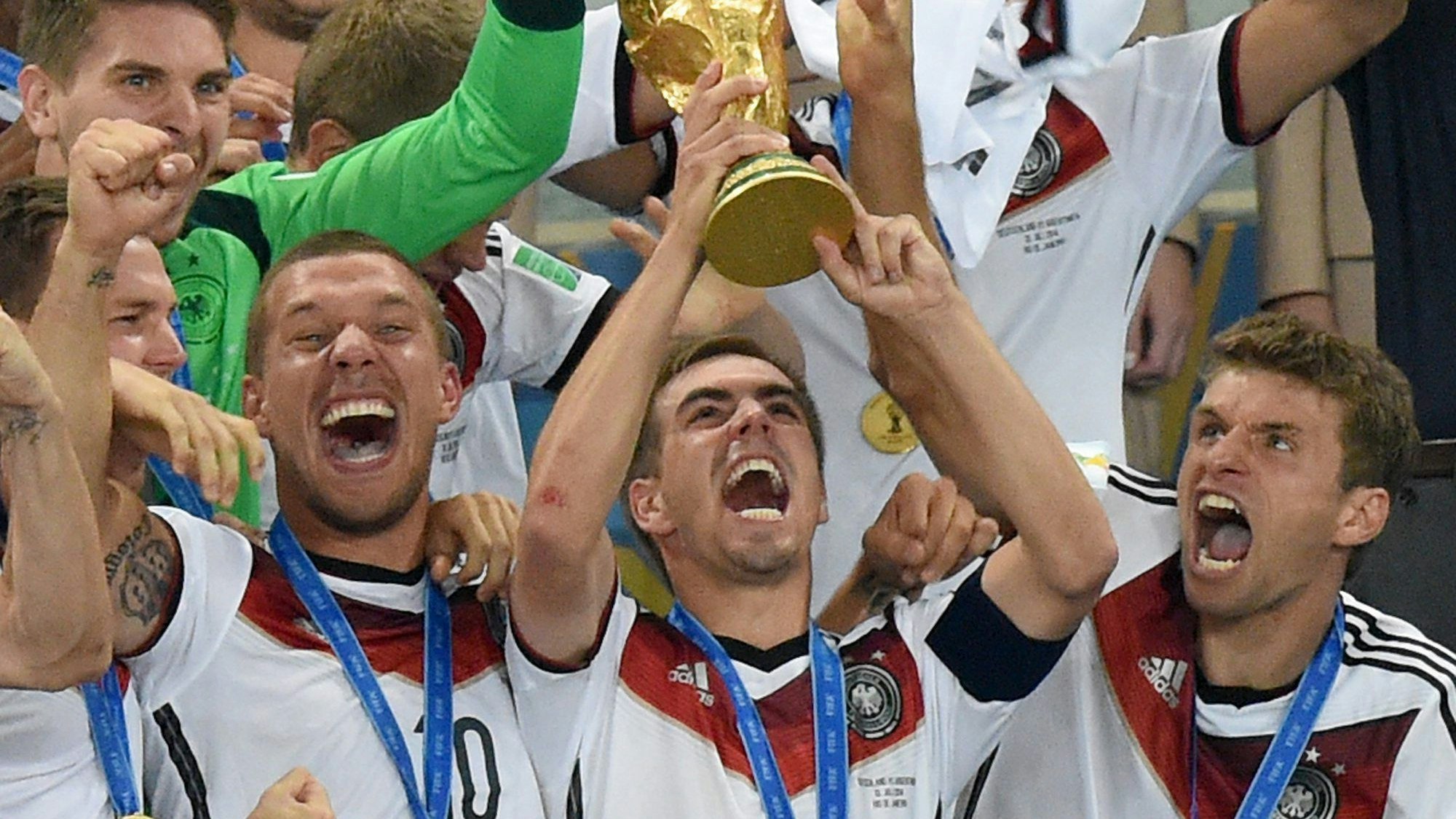 Philipp Lahm jubelt mit dem WM-Pokal zwischen seinen Teamkollegen Lukas Podolski und Thomas Müller