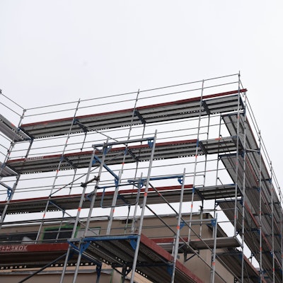 Das Bild zeigt ein an einem Kran schwebendes Modul auf einer Schulbaustelle.