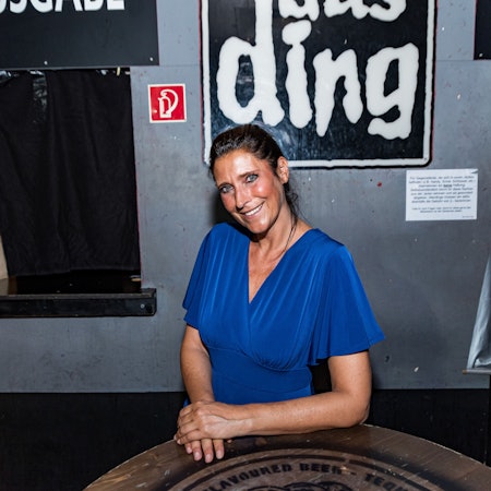 Claudia Wecker, im blauen Kleid, fotografiert im „Studentenclub Das Ding“, den sie betreibt.