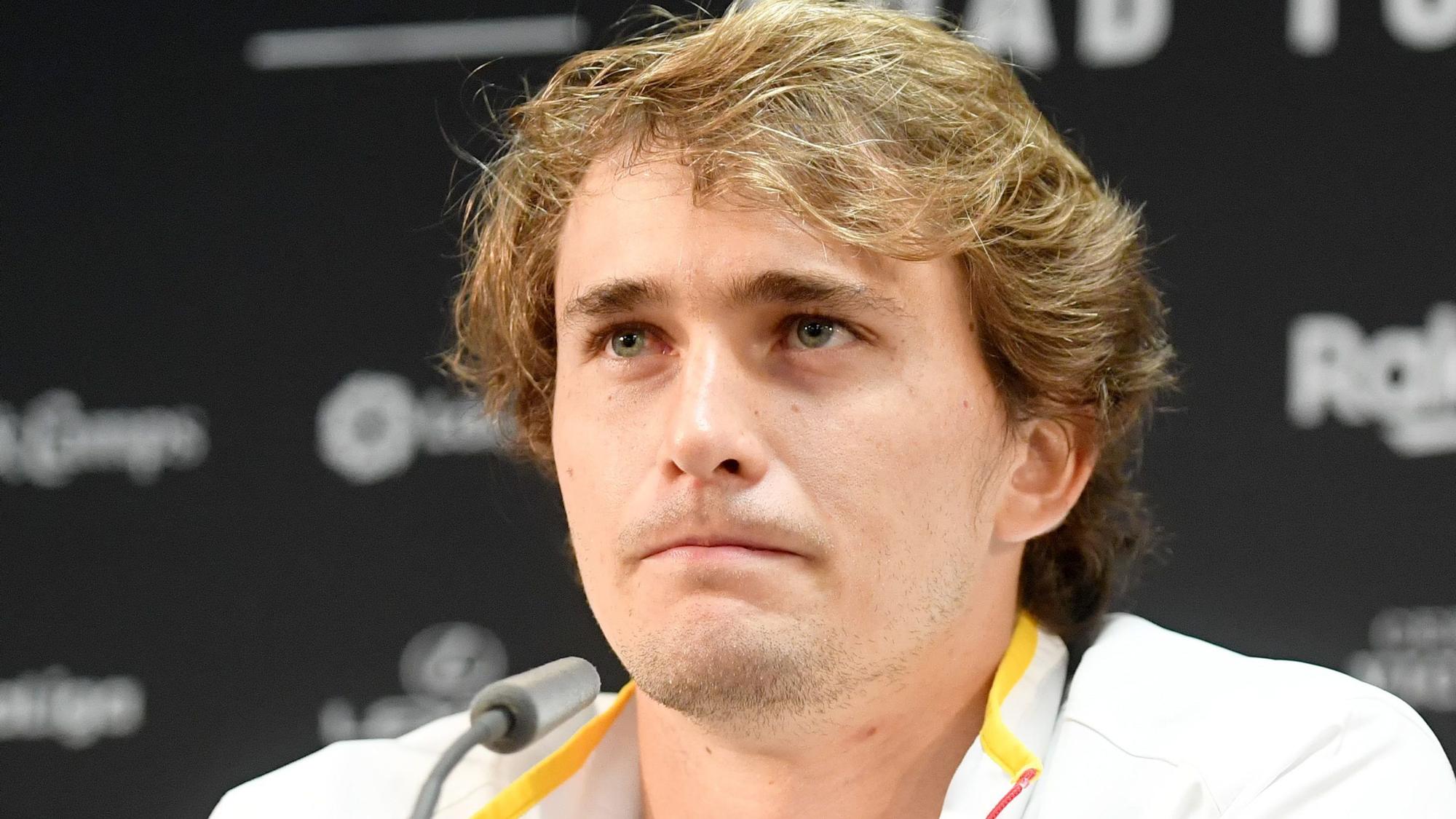 Alexander Zverev sitzt mit ernster Mine vor einem Mikrofon.
