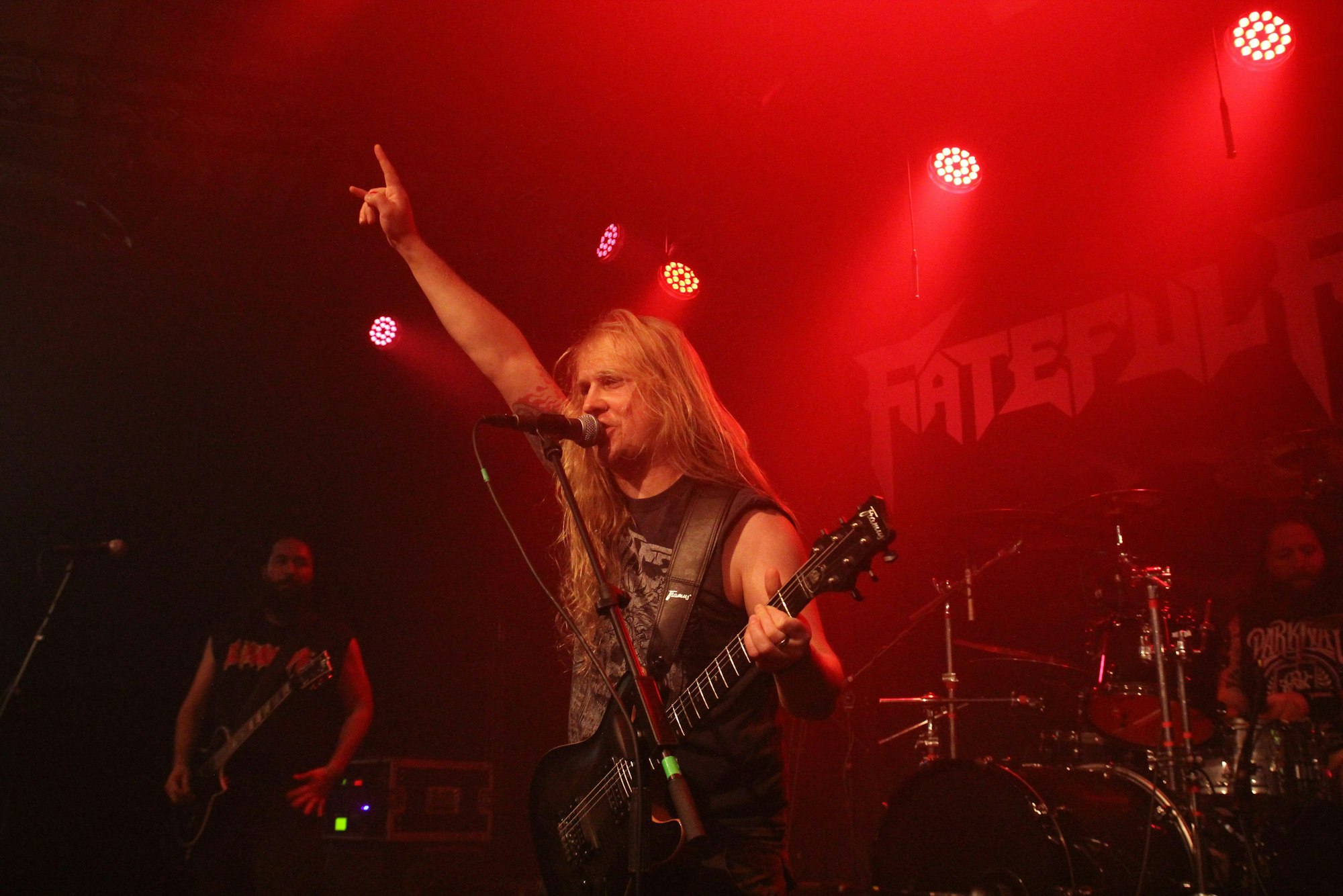 Ein Gitarrist reckt die rechte Hand in die Luft, die Finger zur sogenannten Pommesgabel ausgestreckt.