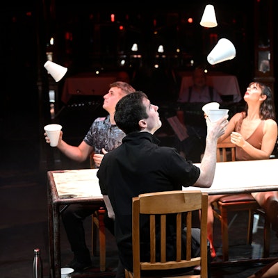 Vier Artisten des jonglieren mit Bechern an einem Tisch.