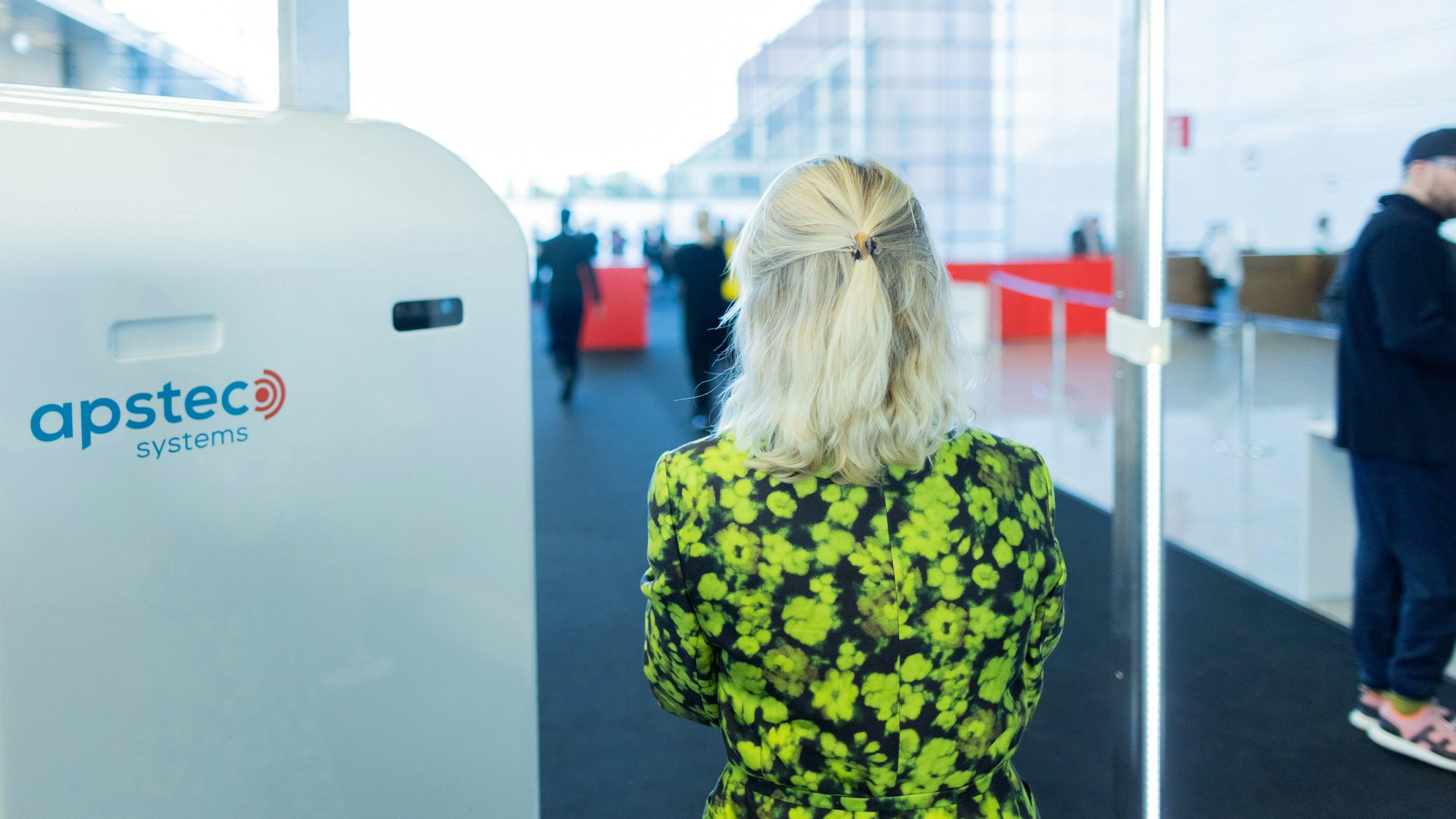 Eine Besucherin der Art Cologne geht im grünen Blumenkleid durch eine Sicherheitskontrolle mit Körperscannern.