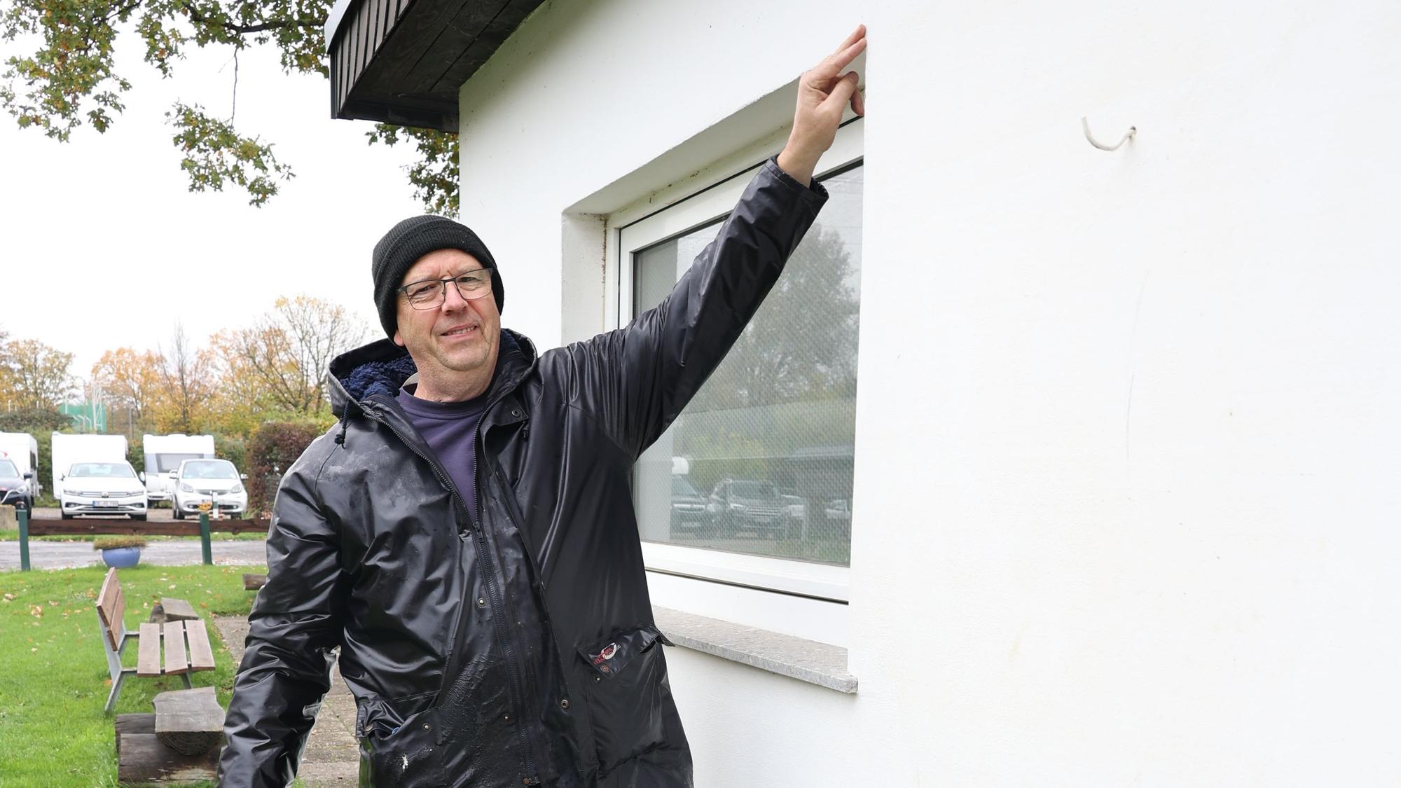 Holger Münstermann in Gummistiefeln zeigt an einem Fenster, wie hoch das Wasser bei der Flut stand, bis zur Oberkante.