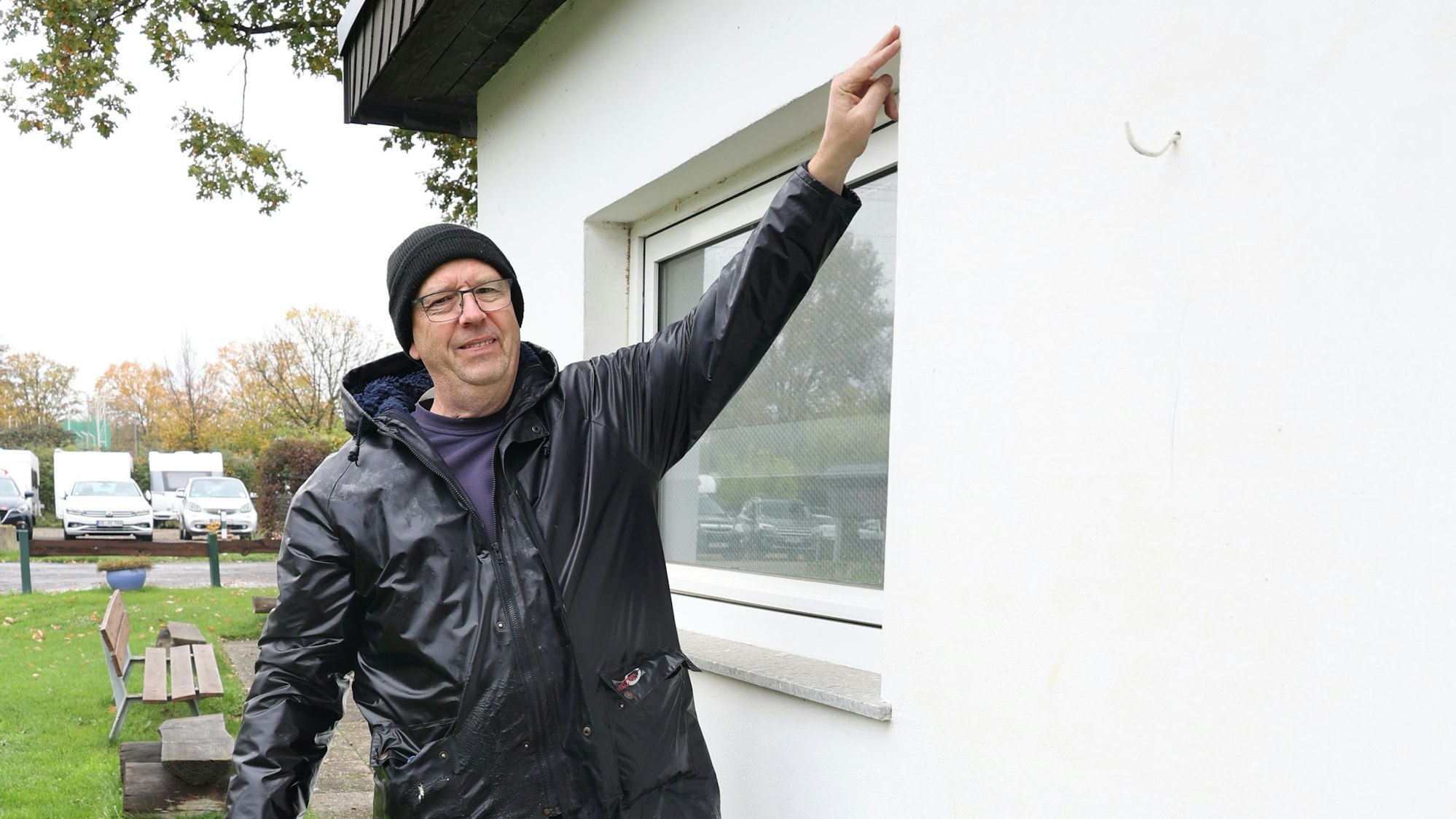 Holger Münstermann in Gummistiefeln zeigt an einem Fenster, wie hoch das Wasser bei der Flut stand, bis zur Oberkante.