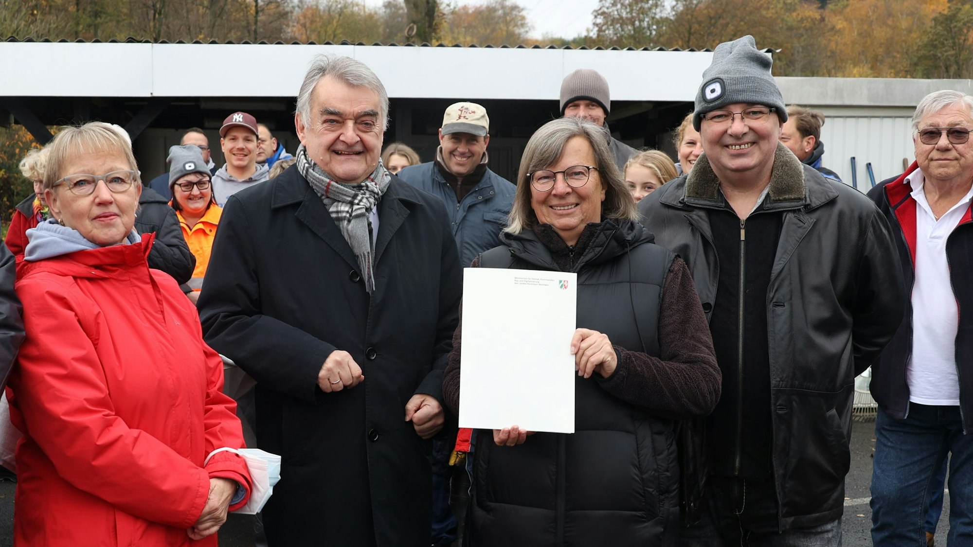 Innenminister Herbert Reul steht mit Kassiererin Dagmar Sapina umringt von Clubmitgliedern auf dem Campingplatz und übergibt den schriftlichen Bescheid über eine halbe Million Euro aus dem Fluthilfe-Fonds.