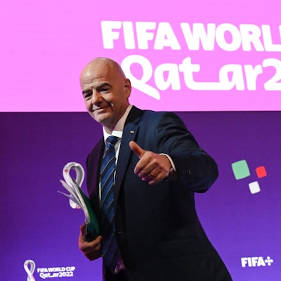 FIFA-Präsident Gianni Infantino steht vor einer Pressewand mit dem Logo der WM 2022 in Katar und hebt den Daumen nach oben.