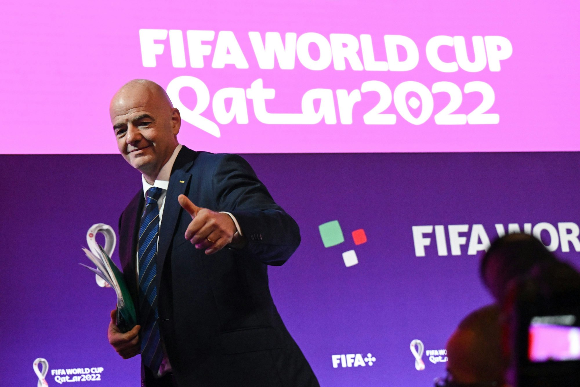 FIFA-Präsident Gianni Infantino steht vor einer Pressewand mit dem Logo der WM 2022 in Katar und hebt den Daumen nach oben.