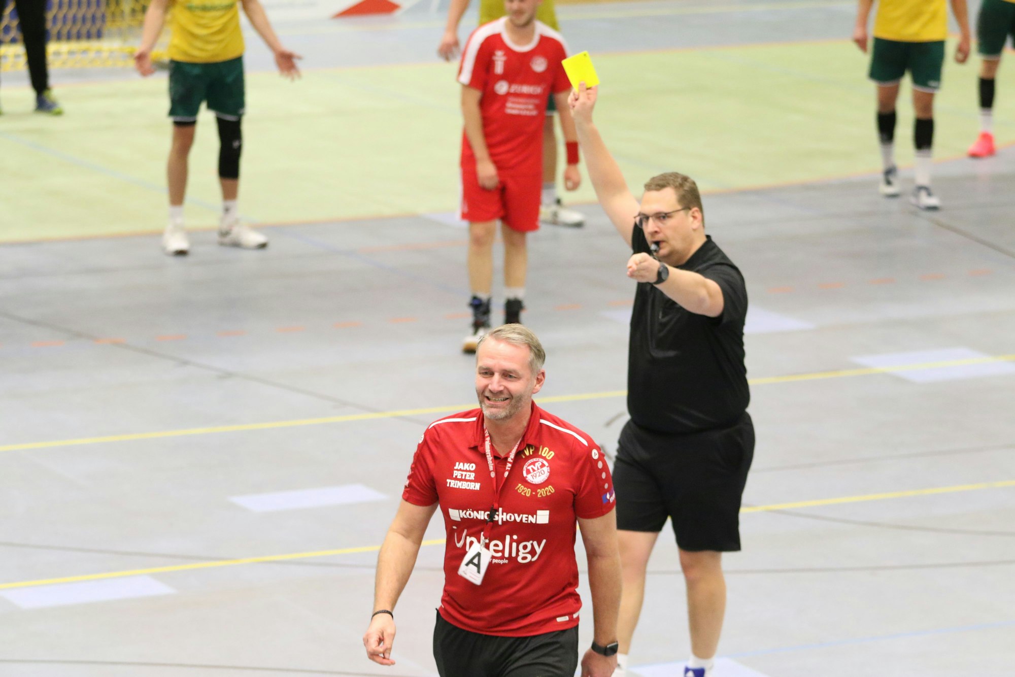 Der Schiedsrichter zeigt Palmersheims Trainer Peter Trimborn die Gelbe Karte. Dieser hat sich bereits vom Unparteiischen mit einem Lächeln auf dem Gesicht abgewandt.