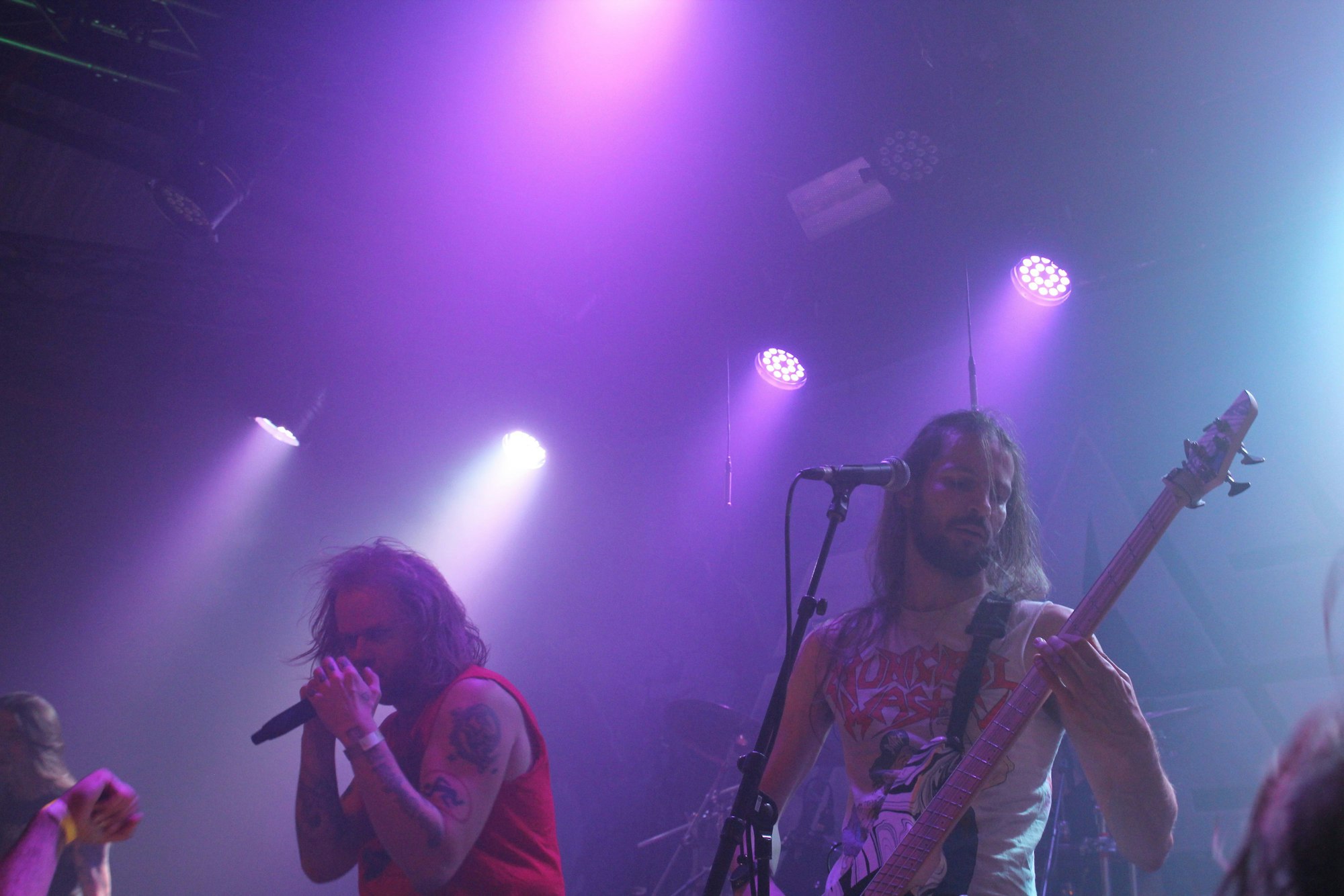 Neben dem Sänger, der sich das Mikrofon dicht vors Gesicht hält, spielt der Bassist.