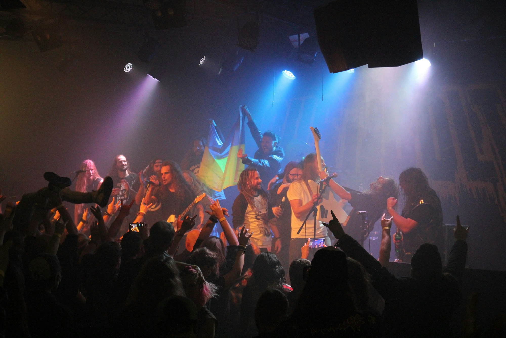 Auf der Bühne stehen viele Musiker, zwei zeigen die ukrainische Flagge.