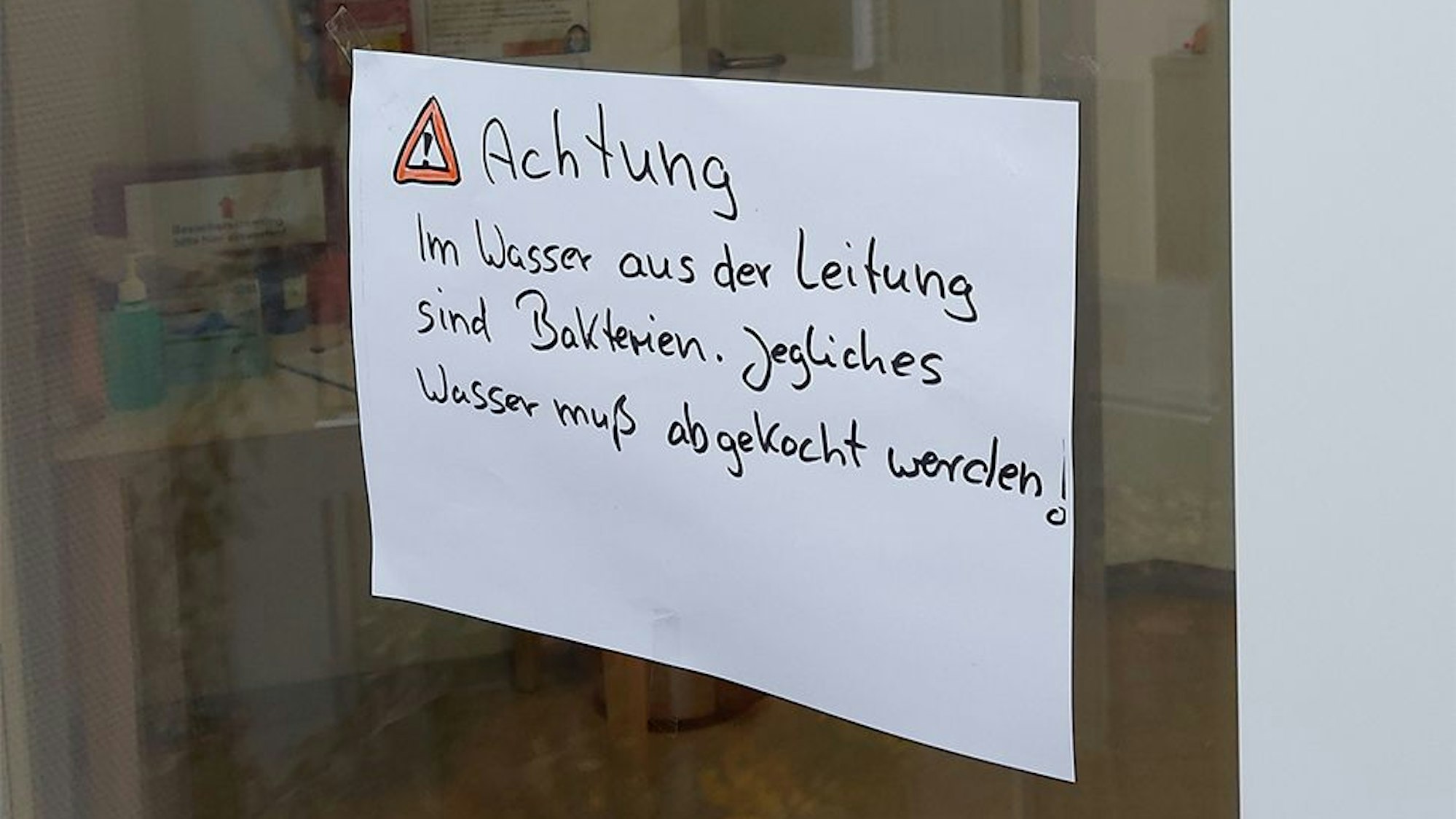 Auf einem Zettel auf einer Glasscheibe steht der Hinweis, dass das Trinkwasser abgekocht werden muss.