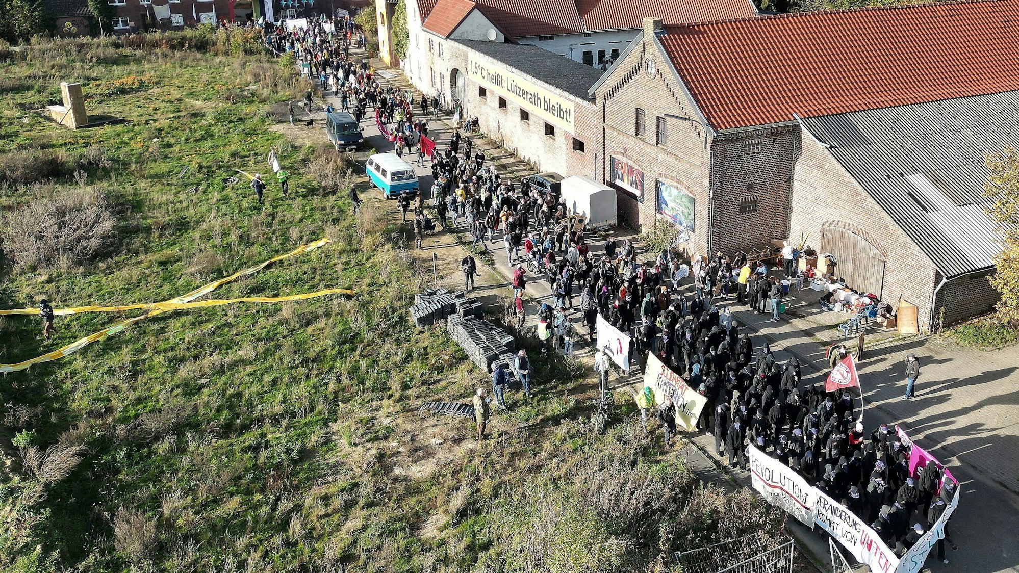 Lützerath von oben gesehen: Bei einer Demonstration in Lützerath ziehen mehrere Hundert Teilnehmer mit Banner durch das Dorf.