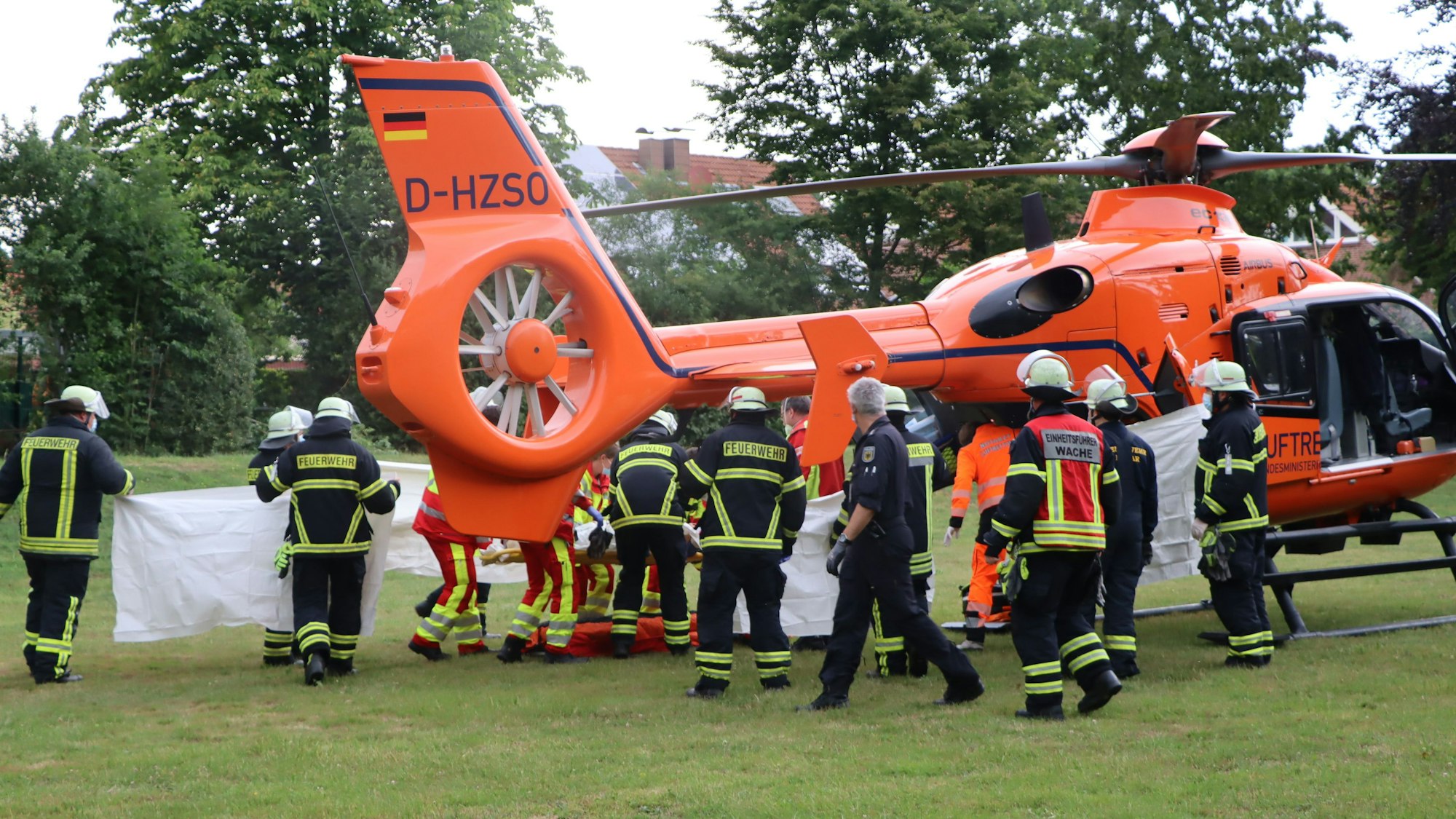 Feuerwehrleute und Rettungssanitäter stehen vor einem Rettungshubschrauber.