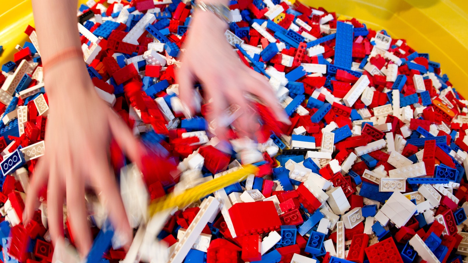 Zwei Hände wühlen in einem bunten Haufen aus Legosteinen.