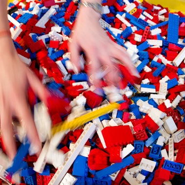 Zwei Hände wühlen in einem bunten Haufen aus Legosteinen.