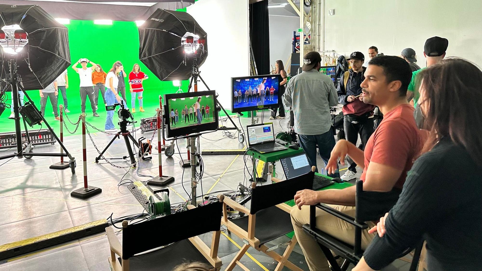 Ein Regisseur blickt auf einen Greenscreen mit mehreren Tänzern.