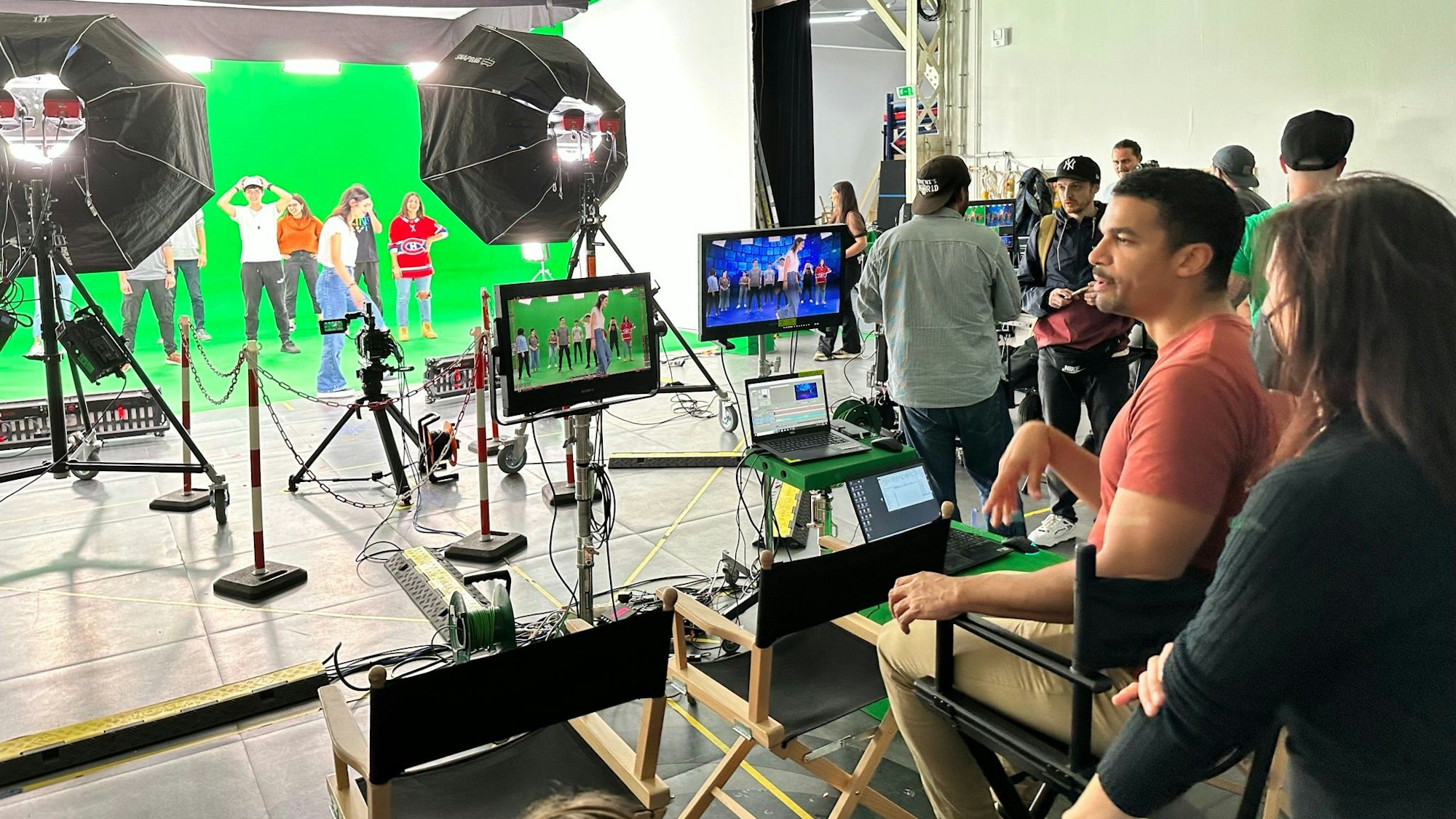 Ein Regisseur blickt auf einen Greenscreen mit mehreren Tänzern.