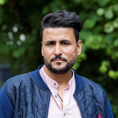 Ibrahim Arslan steht auf einer Straße, im Hintergrund sind Bäume zu sehen. Arslan war sieben Jahre, als zwei Neonazis in Mölln in der Nacht auf den 23. November 1992 erst ein Haus in der Ratzeburg Straße in Brand setzen und wenig später das Wohnhaus seiner Familie in der Mühlenstraße.