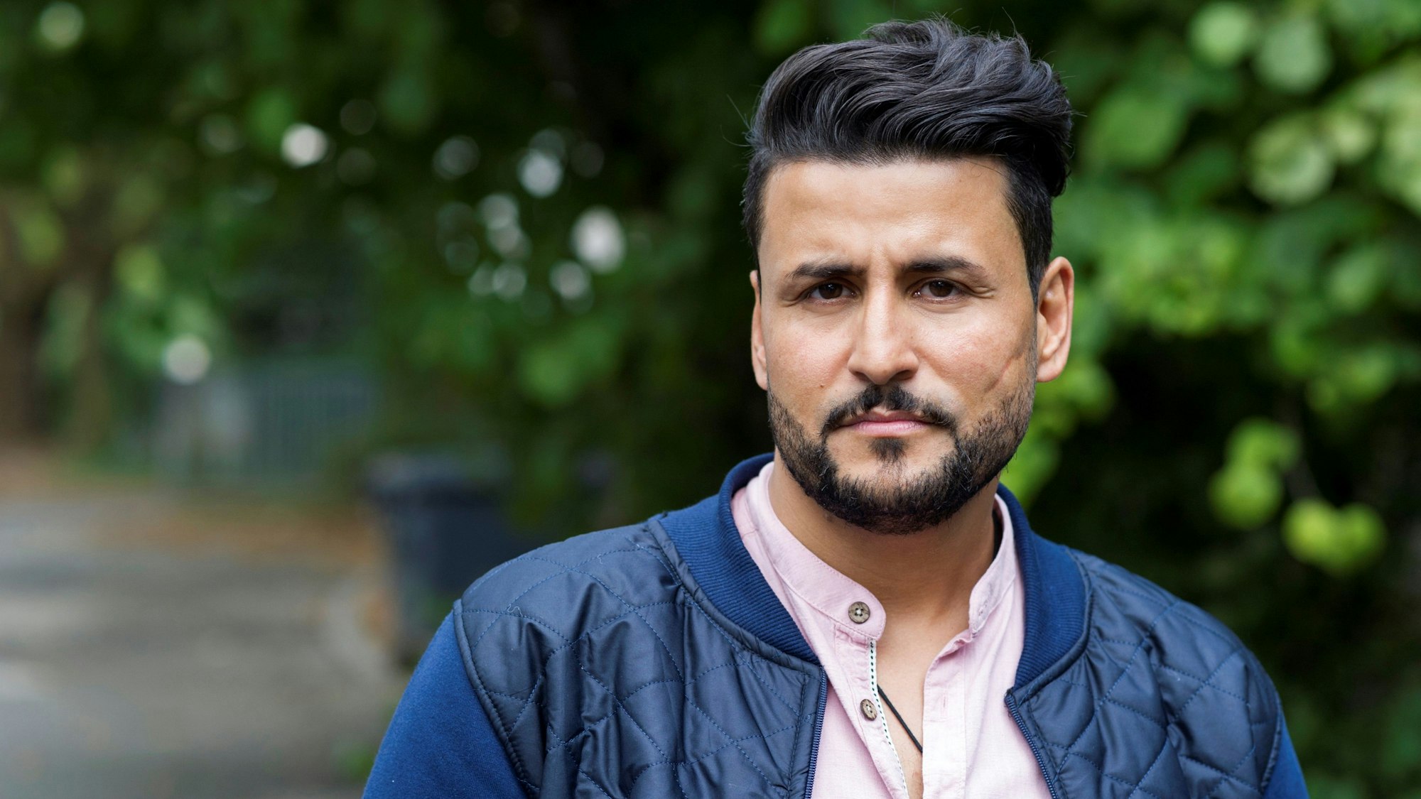 Ibrahim Arslan steht auf einer Straße, im Hintergrund sind Bäume zu sehen. Arslan war sieben Jahre, als zwei Neonazis in Mölln in der Nacht auf den 23. November 1992 erst ein Haus in der Ratzeburg Straße in Brand setzen und wenig später das Wohnhaus seiner Familie in der Mühlenstraße.