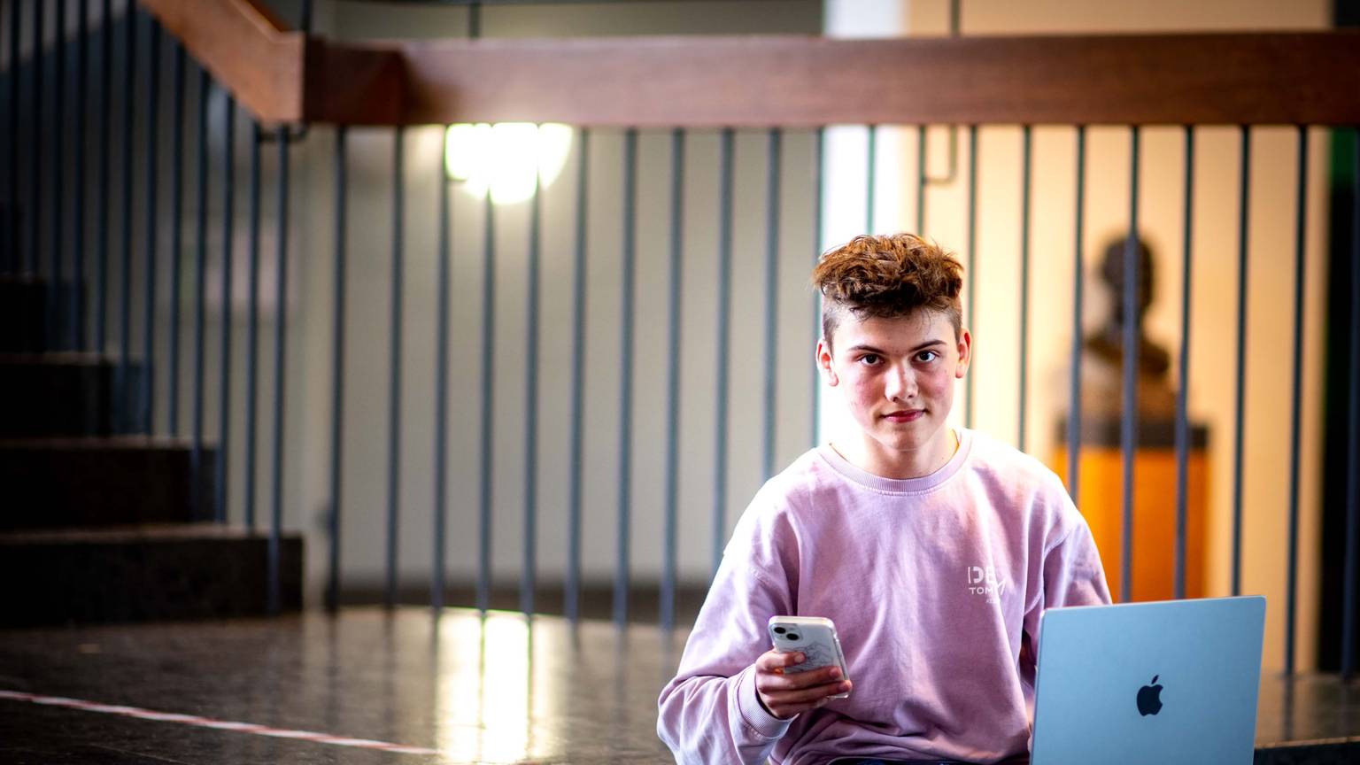 Handy in der Hand, Laptop auf den Beinen. Schüler Noel Dederichs sitzt auf den Stufen des Emil-Fischer-Gymnasiums in Euskirchen.