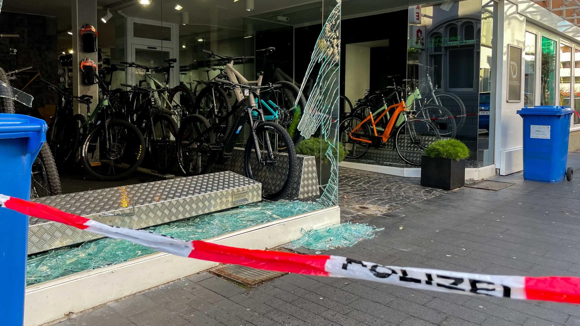Das zertrümmerte Schaufenster eines Fahrradladens. Auf dem Boden und in der Auslage liegen Glasscherben, einige Fahrräder sind noch ausgestellt. Im Vordergrund steht auf weiß-rotem Absperrband das Wort Polizei.