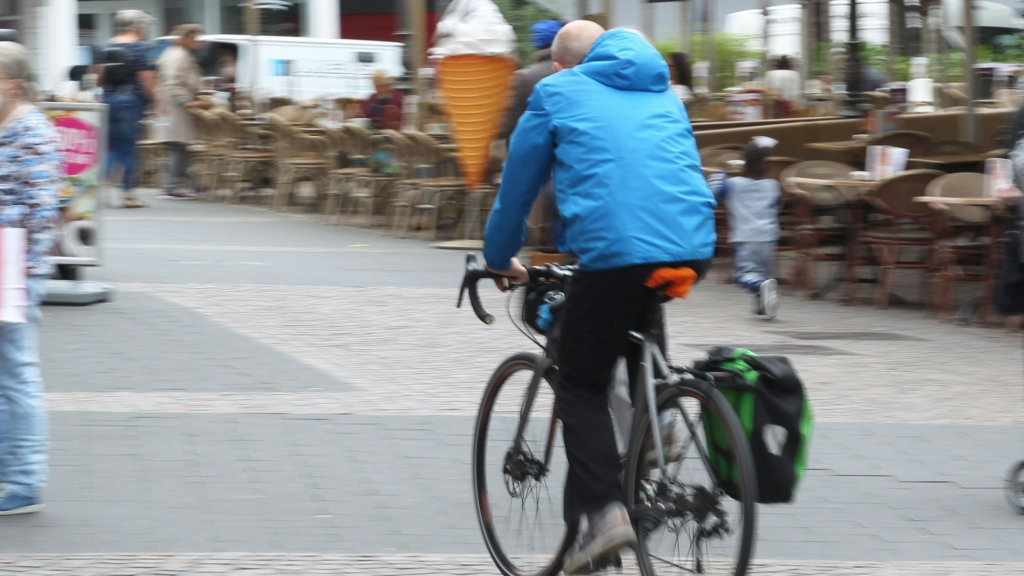 Ein Fahrradfahrer mit einer blauen Jacke radelt in Siegburg über den Markt.