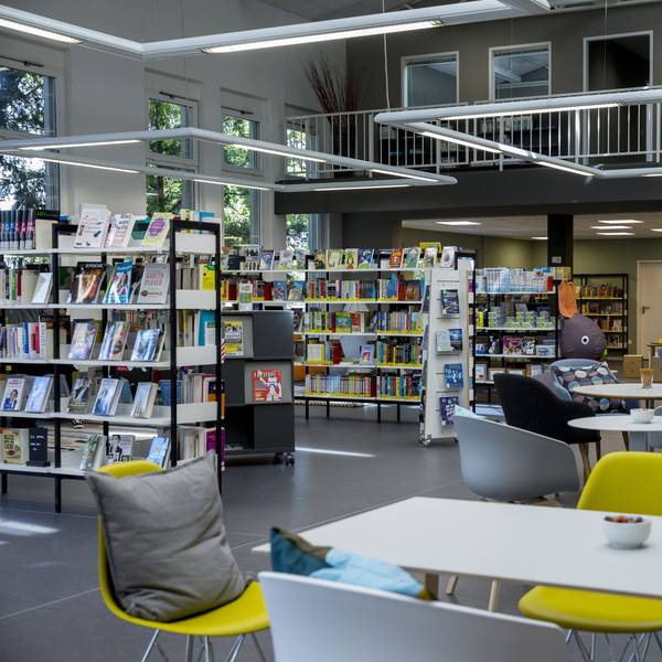 In einem Raum stehen Bücherregale und Tische mit Stühlen wie in einem Café.