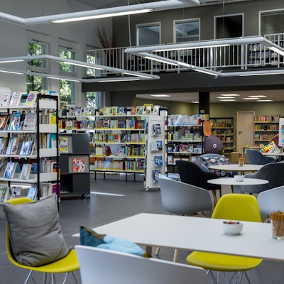 In einem Raum stehen Bücherregale und Tische mit Stühlen wie in einem Café.