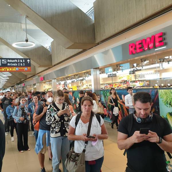 Menschen warten in einer sehr langen Schlange am Flughafen Köln/Bonn für den Check-in und die Sicherheitskontrolle.