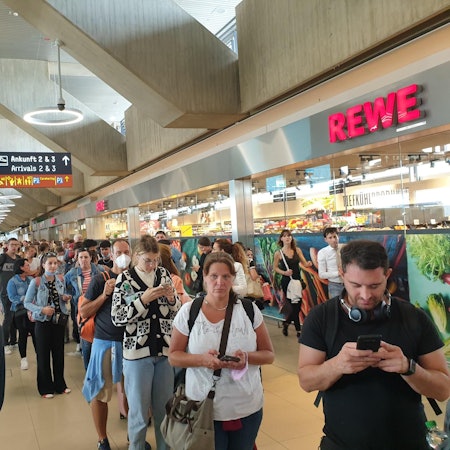 Menschen warten in einer sehr langen Schlange am Flughafen Köln/Bonn für den Check-in und die Sicherheitskontrolle.