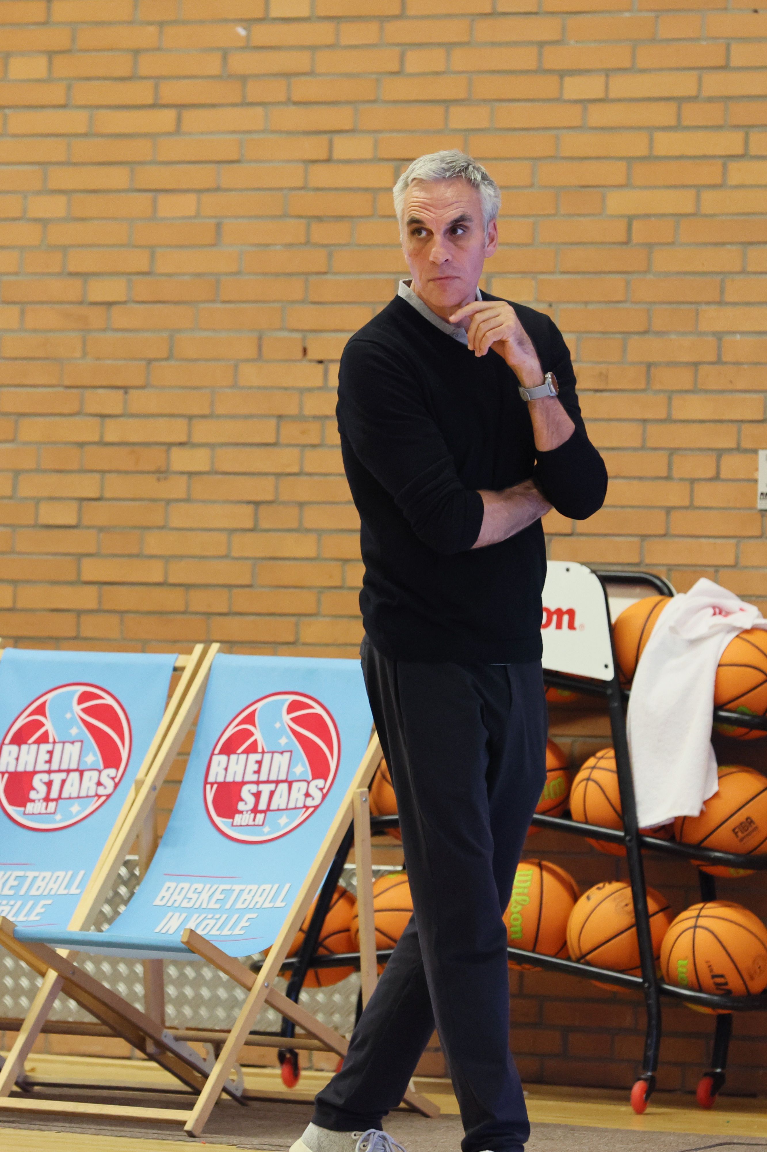 Ein Basketballtrainer steht mit nachdenklicher Miene am Spielfeldrand.