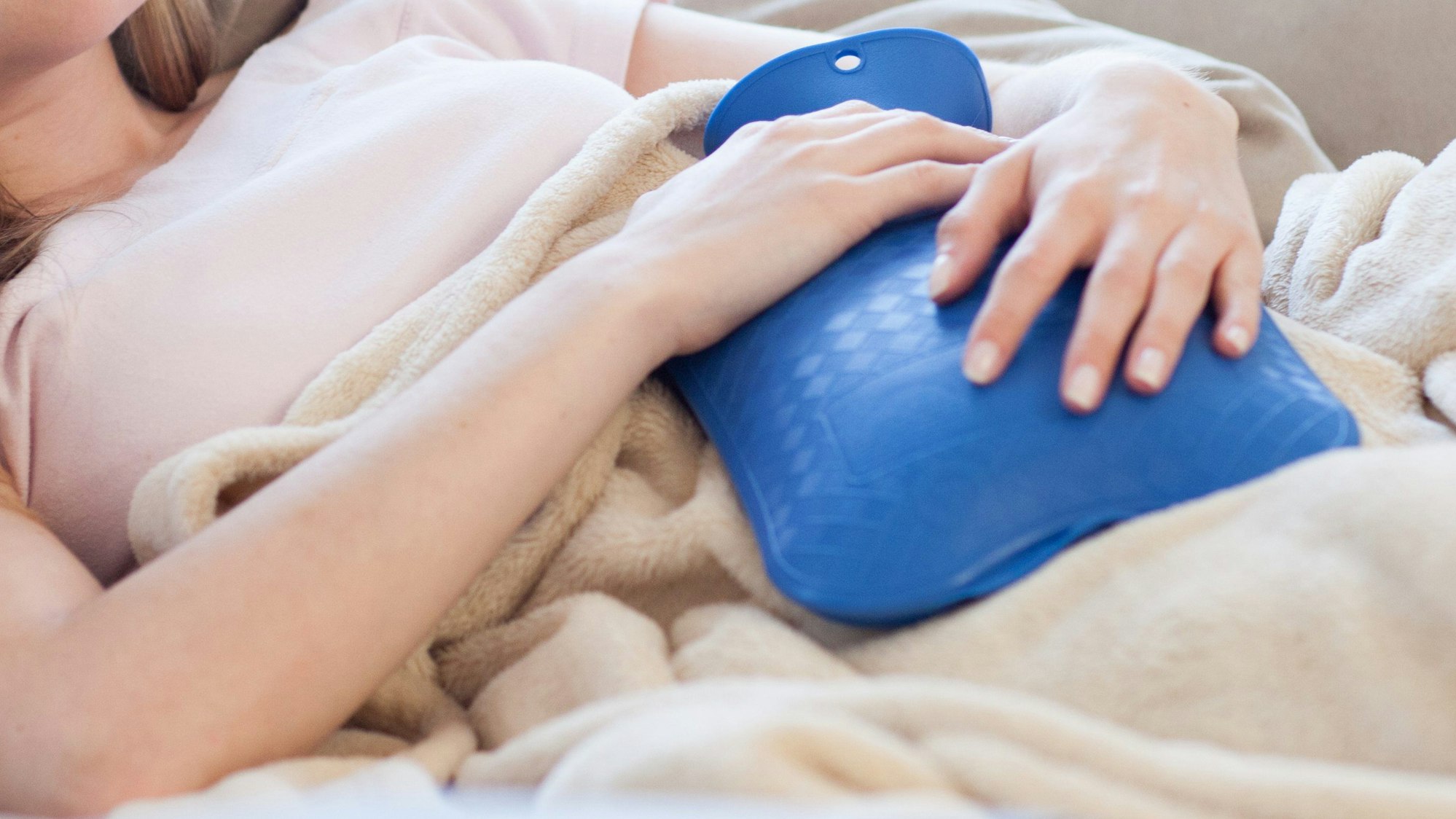 Eine Frau liegt auf der Couch und hält eine Wärmflasche.
