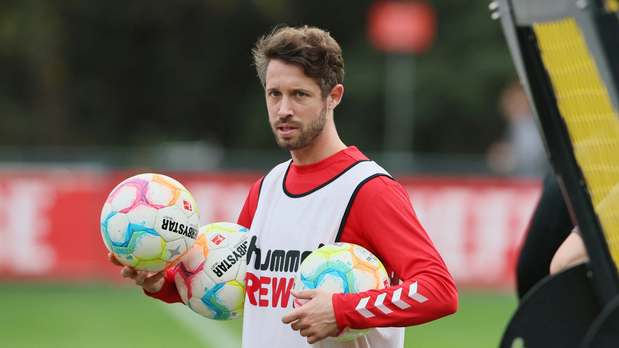 Mark Uth vom 1.FC Köln beim Training am Geißbockheim. Er hält drei Bälle in der Hand und trägt das rot-weiße Trainingsoutfit des 1. FC Köln.