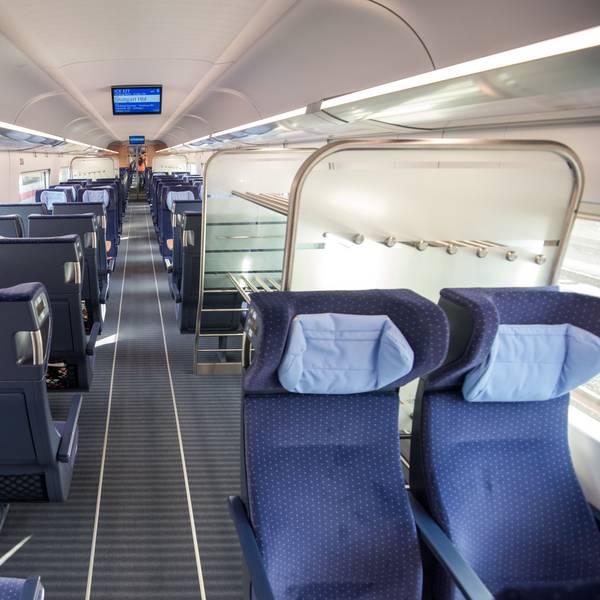 Ein ICE der Deutschen Bahn. Zu sehen sind mehrere blaue Sitze und eine Kofferablage in einem leeren Abteil.