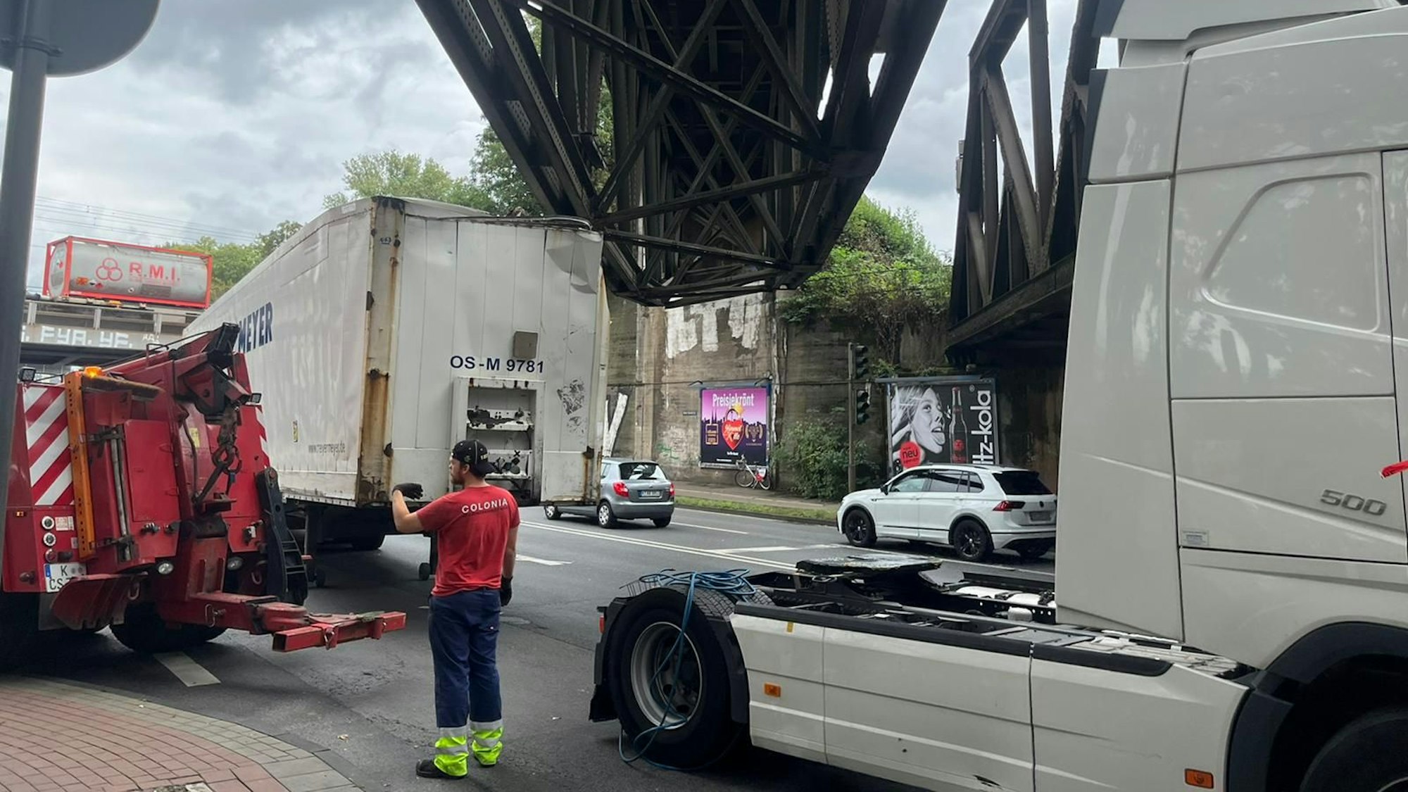 Ein Lkw steckt unter einer Brücke, ein Mitarbeiter eines Abschleppunternehmens steht davor.