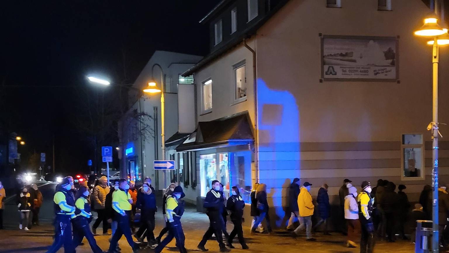 Blick auf Menschen, die in der Dunkelheit einen Zug bilden und dabei von Polizisten begleitet werden.