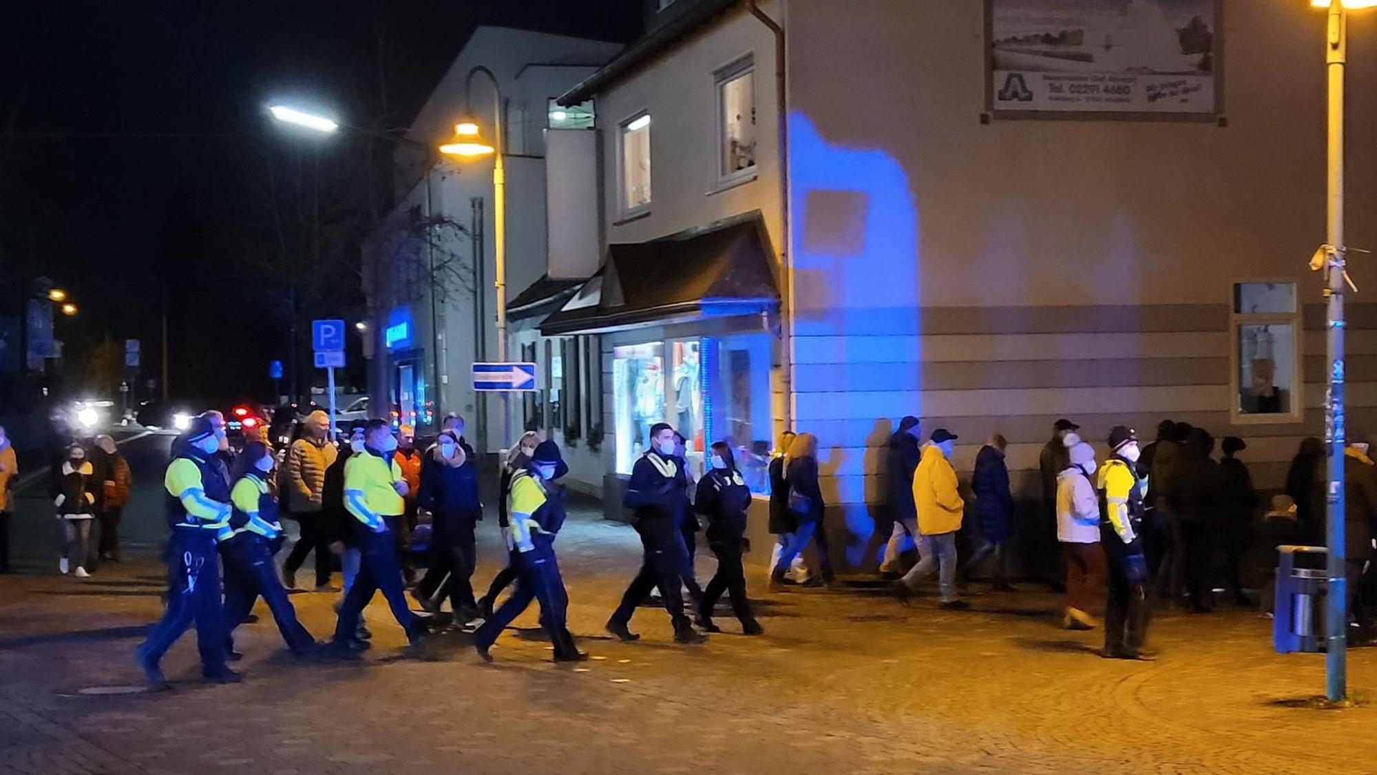 Blick auf Menschen, die in der Dunkelheit einen Zug bilden und dabei von Polizisten begleitet werden.