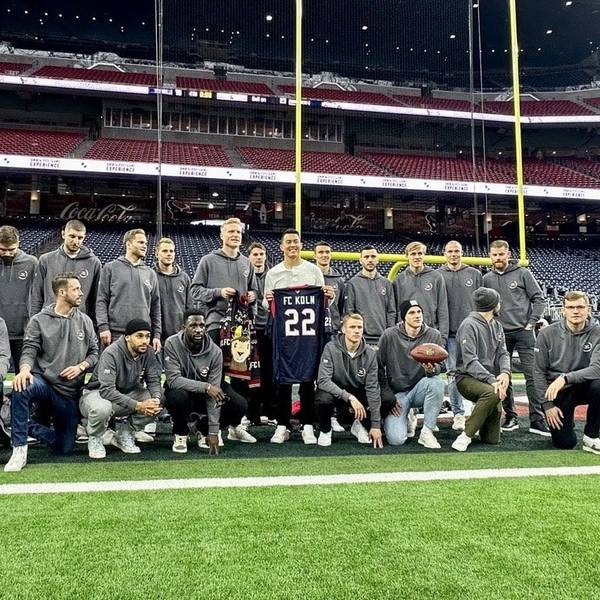 Die Spieler des 1. FC Köln haben sich mit Ka'imi Fairbairn, dem Kicker der Houston Texans, auf dem Rasen des NRG-Stadions von Houston zum Gruppenbild aufgestellt. Fairbairn überreicht den Kölnern ein Trikot der Texans mit „FC Köln“ und der Nummer 22 darauf.
