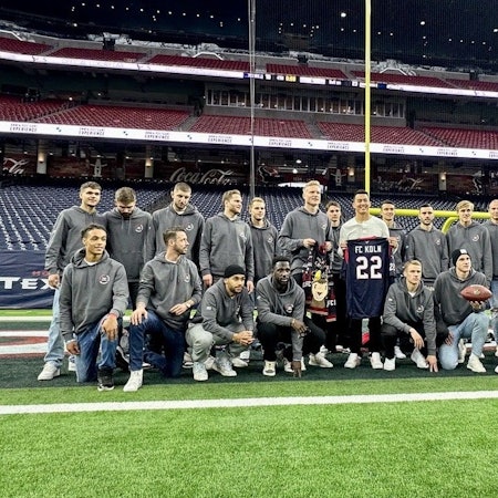 Die Spieler des 1. FC Köln haben sich mit Ka'imi Fairbairn, dem Kicker der Houston Texans, auf dem Rasen des NRG-Stadions von Houston zum Gruppenbild aufgestellt. Fairbairn überreicht den Kölnern ein Trikot der Texans mit „FC Köln“ und der Nummer 22 darauf.