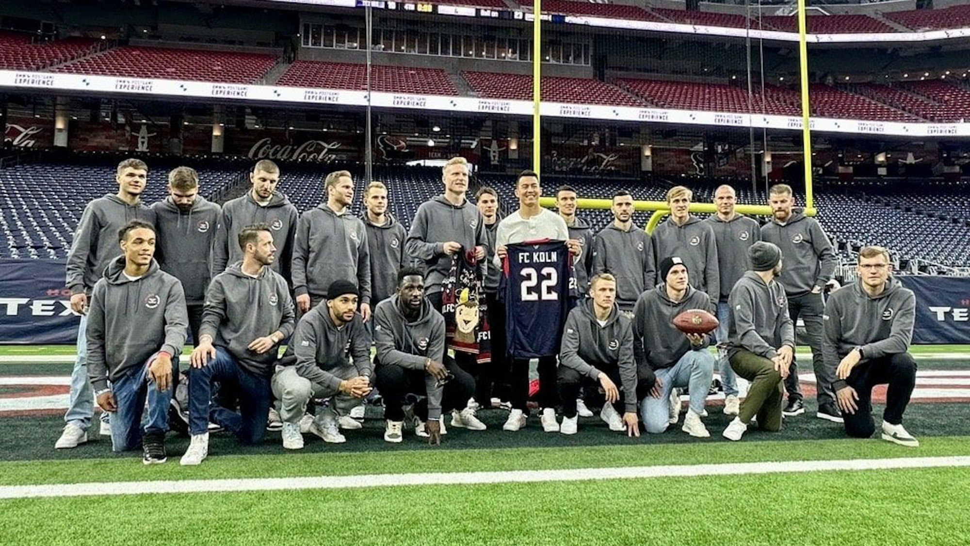 Die Spieler des 1. FC Köln haben sich mit Ka'imi Fairbairn, dem Kicker der Houston Texans, auf dem Rasen des NRG-Stadions von Houston zum Gruppenbild aufgestellt. Fairbairn überreicht den Kölnern ein Trikot der Texans mit „FC Köln“ und der Nummer 22 darauf.