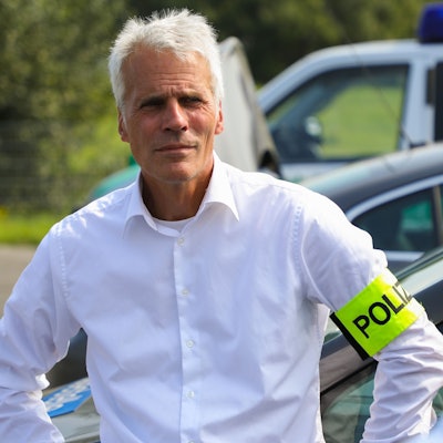 Dirk Weinspach ist bei einem Einsatz zu sehen. Er trägt ein weißes Hemd und eine neongelbe Polizei-Binde am Arm.