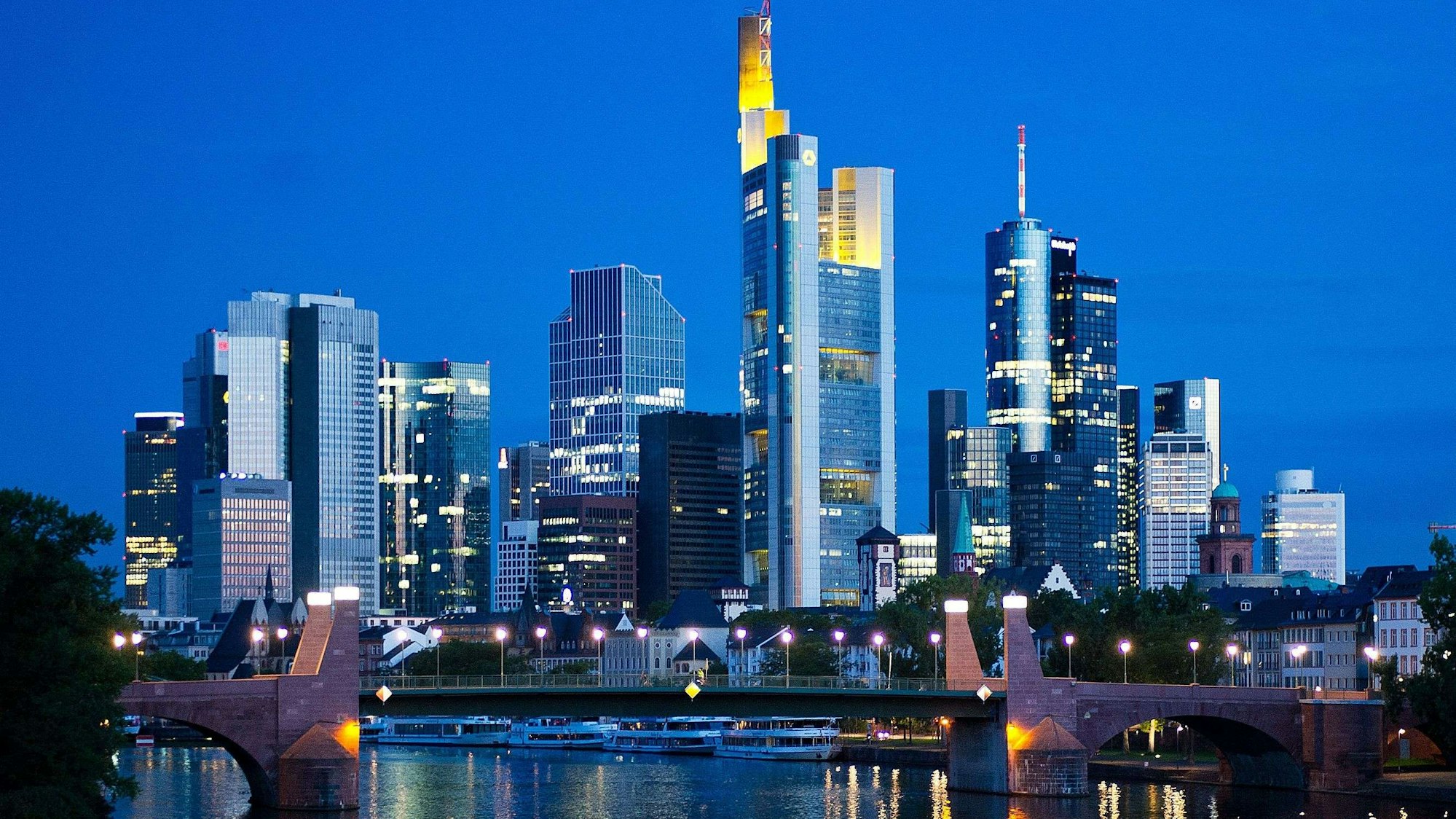 ARCHIV - Im ersten Licht des Tages spiegeln sich am 26.08.2015 die Lichter der Skyline von Frankfurt am Main (Hessen) im Wasser des Mains. Foto: Christoph Schmidt/dpa