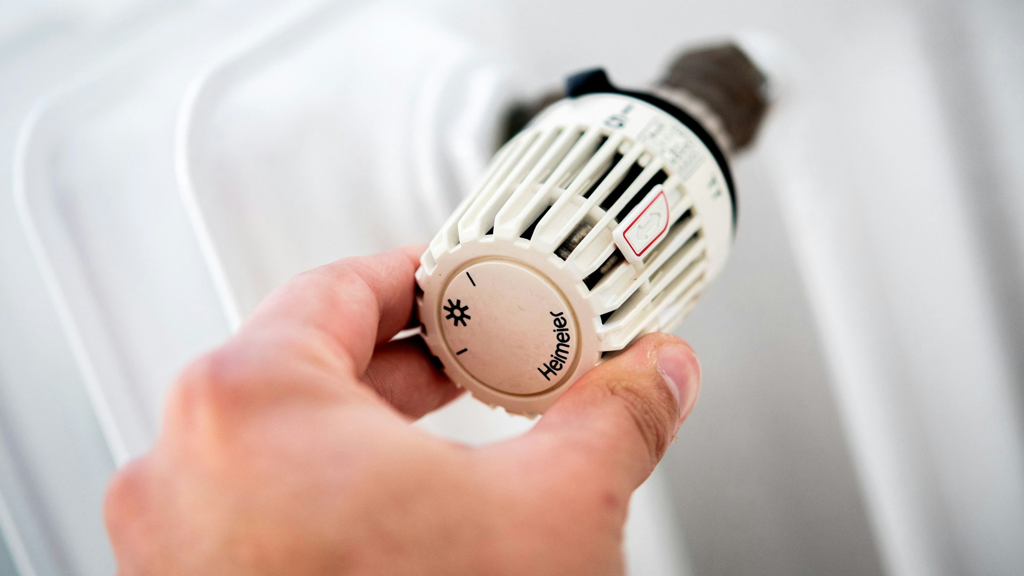 Ein Mann dreht in einer Wohnung am Thermostat einer Heizung.