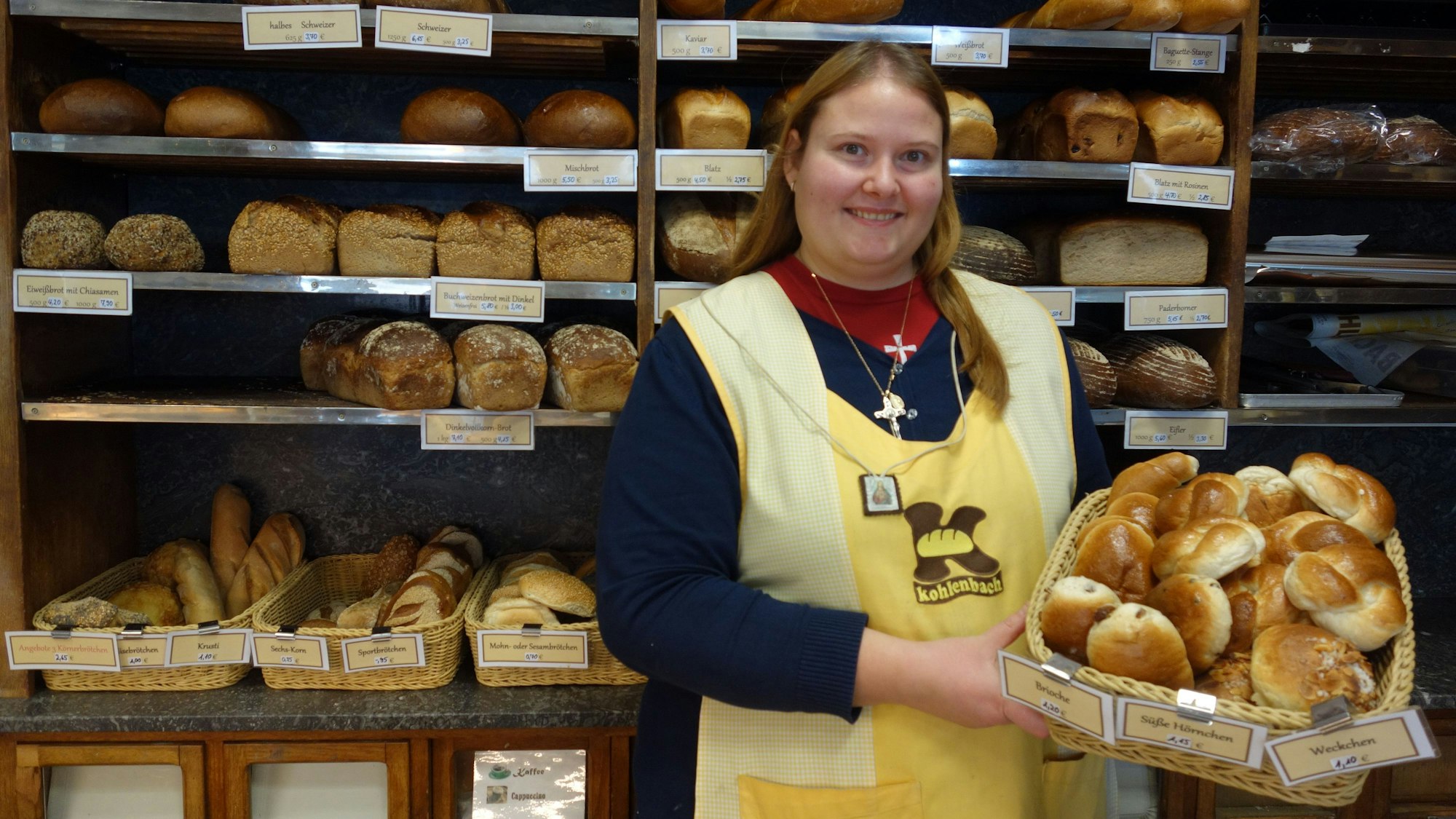 Eine Verkäuferin der Bäckerei Kohlenbach hält einen Korb voll Weckchen. Im Hintergrund ist eine gefüllte Brotauslage zu sehen.