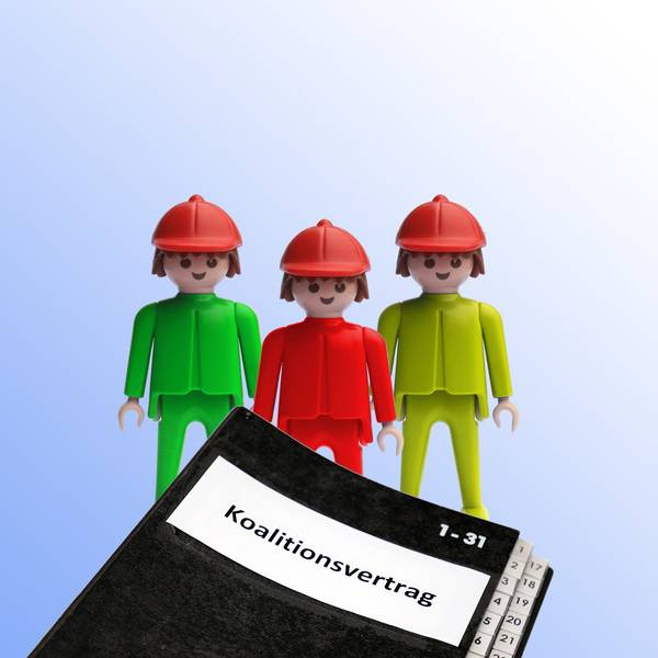 Ein grüner, ein roter und ein gelber Playmobilmensch stehen hinter einer Mappe mit der Aufschrift „Koalitionsvertrag“.