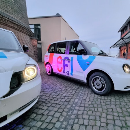 Ein Efi-Kleinbus mit Platz für sechs Fahrgäste steht auf dem Platz vor dem Funkenturm in Opladen.