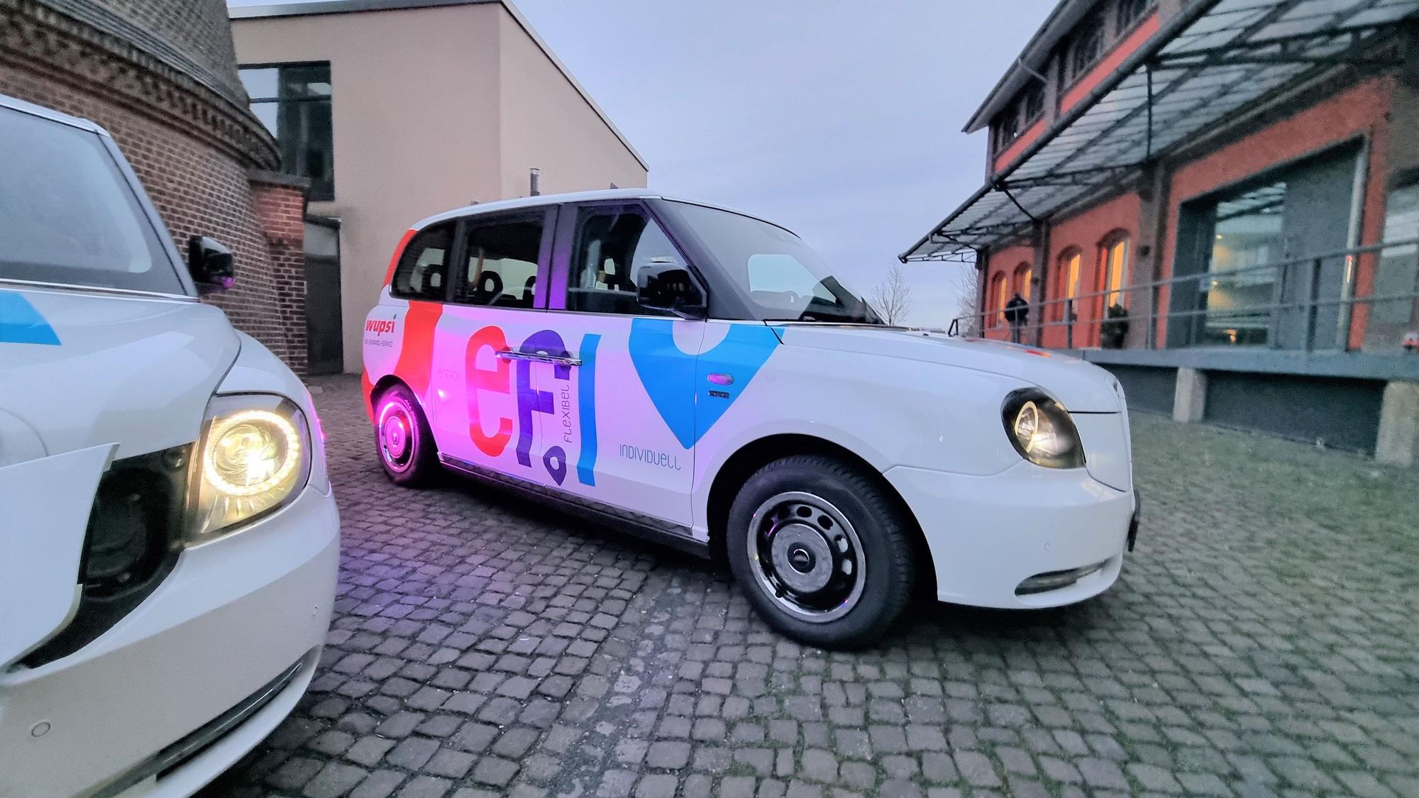 Ein Efi-Kleinbus mit Platz für sechs Fahrgäste steht auf dem Platz vor dem Funkenturm in Opladen.